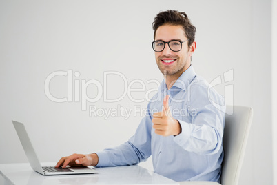 Businessman showing thumbs up while using laptop Businessman showing thumbs up while using laptop