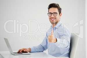 Businessman showing thumbs up while using laptop