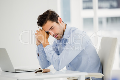 Tensed businessman sitting at table with laptop