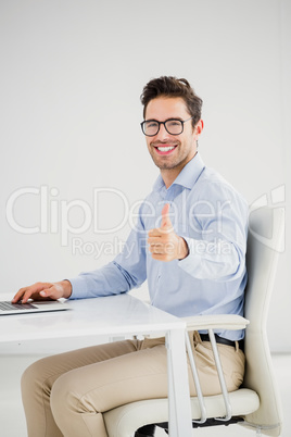 Businessman showing thumbs up while using laptop