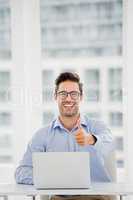 Businessman showing thumbs up while using laptop