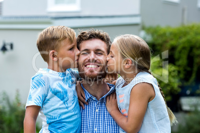 Children kissing smiling father at yard