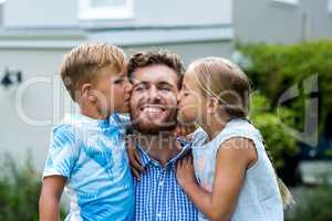 Children kissing smiling father at yard