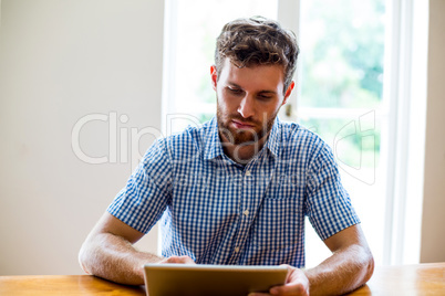 Happy man using digiatl tablet while sitting at table