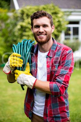 Smiling man carrying garden hose in yard
