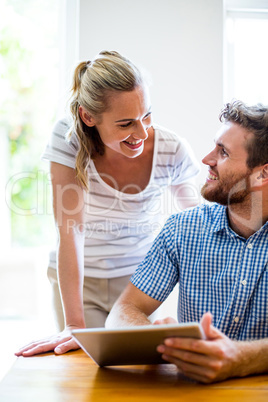 Smiling man showing digiatl tablet to woman at home