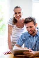 Woman standing by man using tablet at home