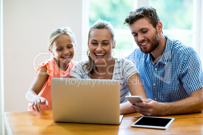 Happy mother with daughter and father using laptop