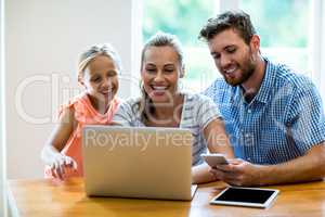 Happy mother with daughter and father using laptop