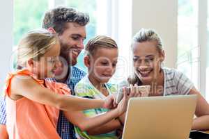 Children showing phone to parents sitting with laptop at table