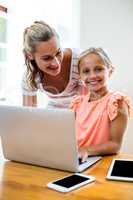 Mother with smiling daughter using laptop at home