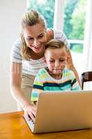 Smiling mother and son using laptop at home