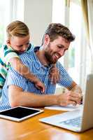 Smiling son leaning on father working at home