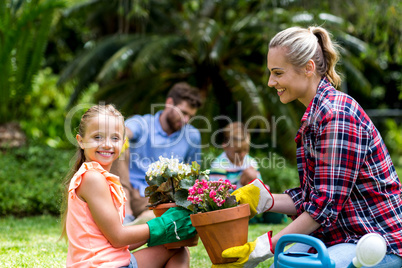 Mother giving flower pot to smiling daughter at yard