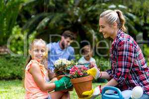 Mother giving flower pot to smiling daughter at yard