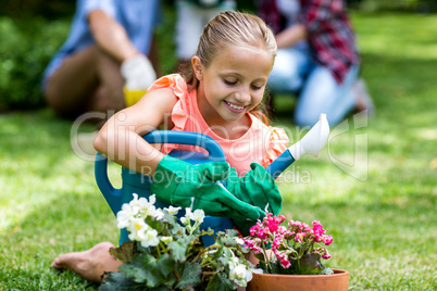 Girl holding watering can by flower pots at yard