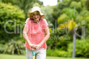 Senior woman in hat standing with rake at yard