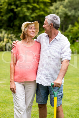 Senior couple holding rake while standing in yard