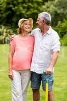 Senior couple holding rake while standing in yard