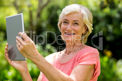 Smiling senior woman holding tablet in yard