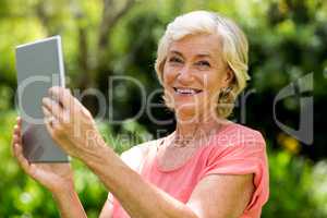 Smiling senior woman holding tablet in yard