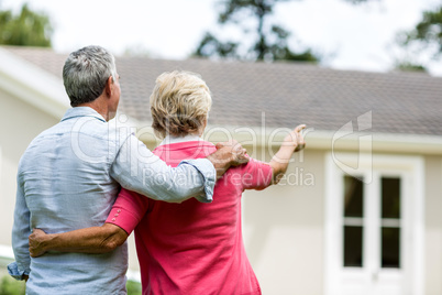 Senior couple looking at house while standing ih yard