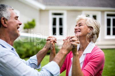Happy senior couple holding hands outside house in yard