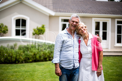 Senior couple with arms around standing in yard