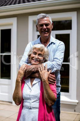Smiling senior couple standing with arms around at yard