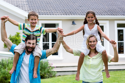 Happy parents carrying children on shoulder at yard