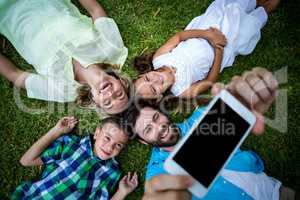 Happy family taking selfie while lying on grass in yard