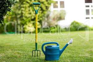 Close-up of rake and watering can in yard