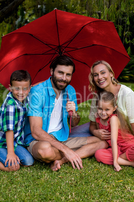 Smiling family sitting with umbrella in yard