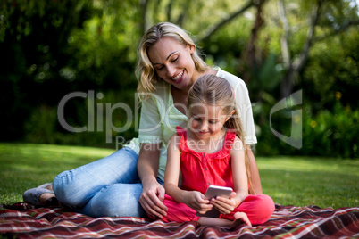 Mother looking at daughter using phone in yard