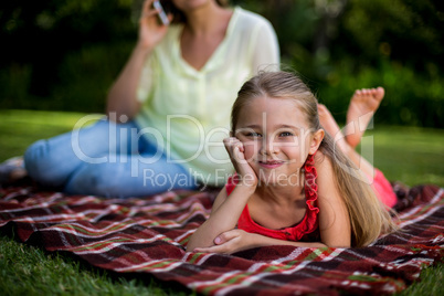 Girl lying on blanket while mother sitting in background