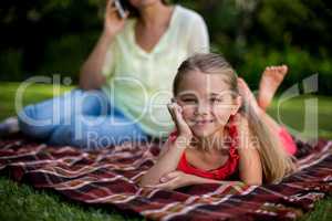 Girl lying on blanket while mother sitting in background