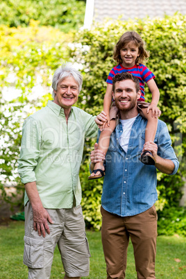 Grandfather standing with son carrying grandson at yard