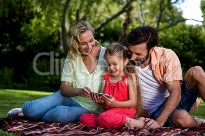 Happy parents with daughter looking at mobile phone in yard