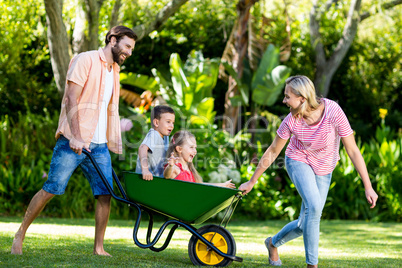 Parents pushing children sitting in wheelbarrow at yard