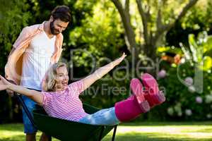 Man pushing woman sitting in wheelbarrow at yard