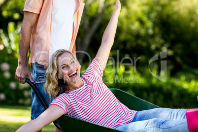 Man pushing woman sitting in wheelbarrow at yard