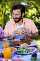 Happy man sitting with sandwich at table in yard
