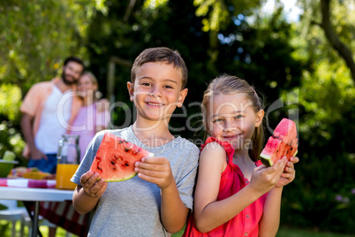 Siblings holding watermelon with parents at yard