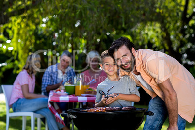 Smiling father with son by barbecue grill in yard