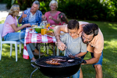 Father teaching son cooking on barbecue with family