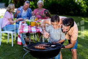 Father teaching son cooking on barbecue with family