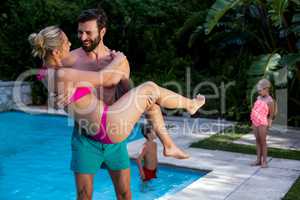 Man carrying woman at poolside with children in background