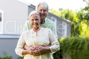 Senior couple embracing against house
