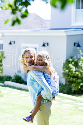 Mother piggy-backing daughter in yard