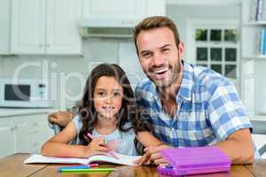 Happy father with daughter writing in book at table